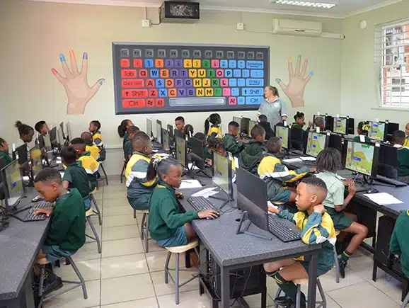 A classroom full of kids sitting in front of computers while they learn how to use the keyboard and letters at a PnS Academy.